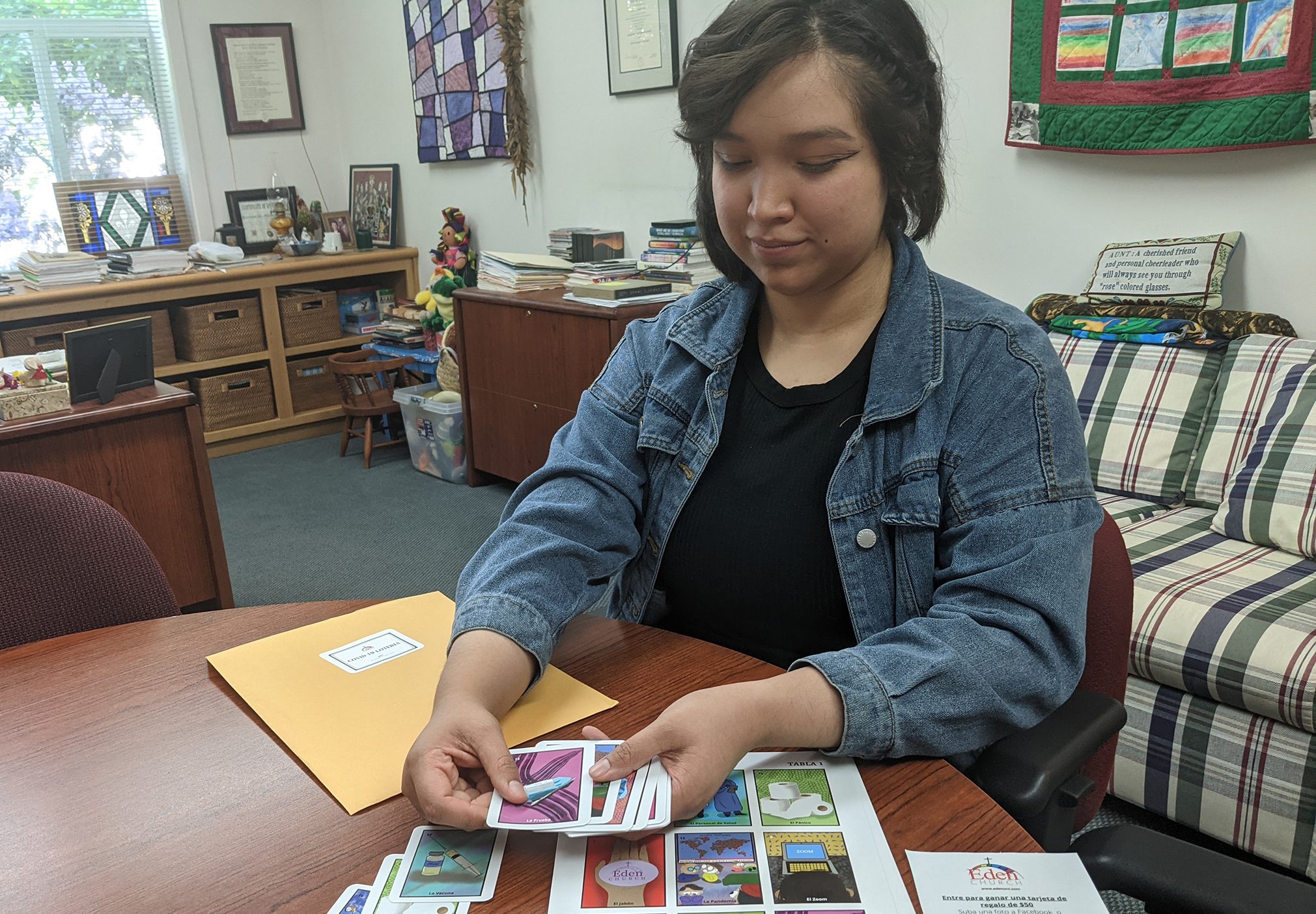 Karen Victorio sits at a desk and distributes COVID-10 themed loteria cards
