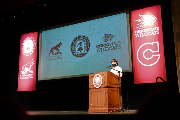 President Hutchinson stands on stage next to banners of our new logos.