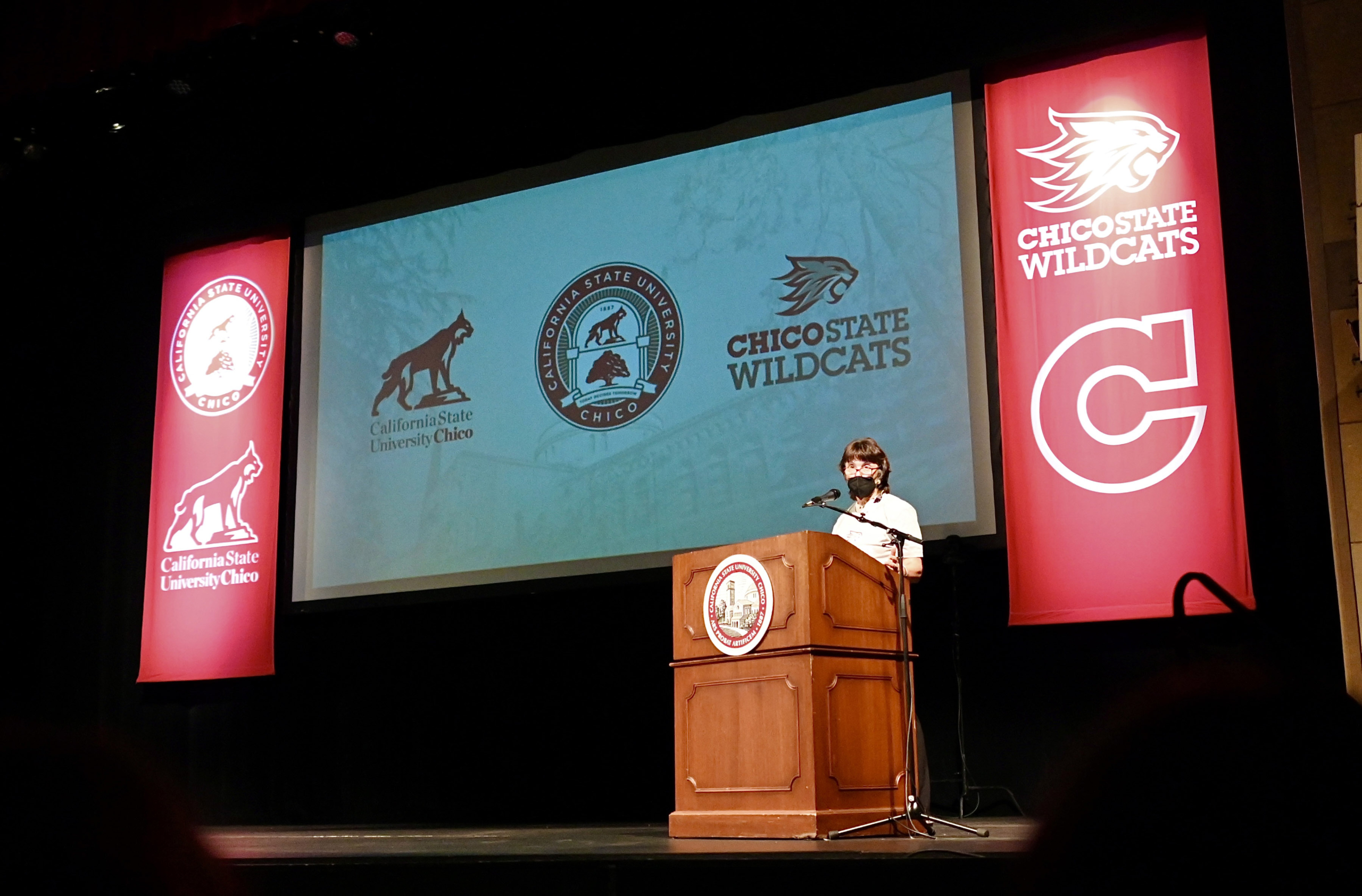 President Hutchinson stands on stage next to banners of our new logos.