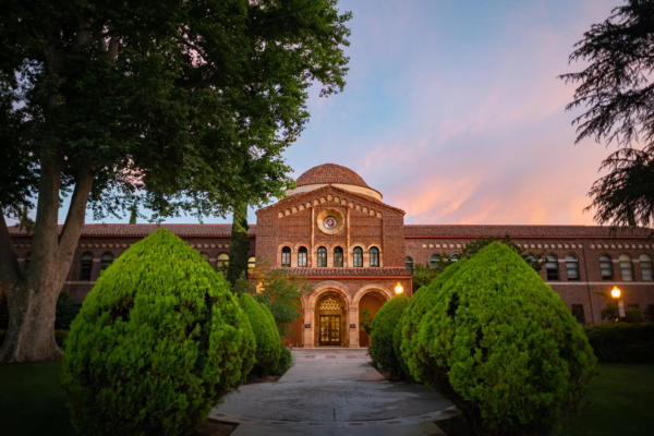 An academic building sits in the early evening sun with colorful clouds swirling behind.