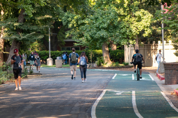 Students walk and ride bicycles on a college campus.