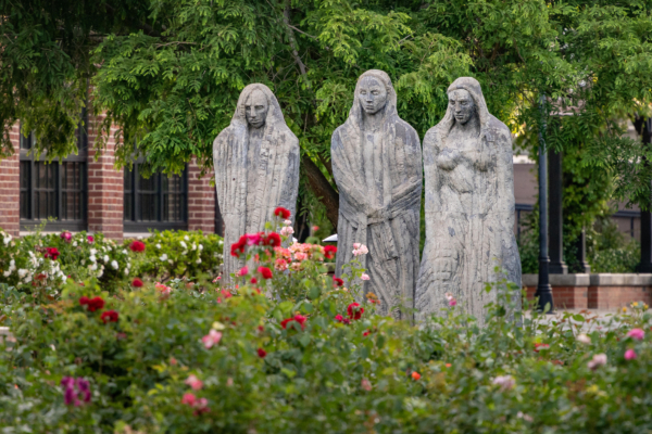 Three tall stone statues loom over a rose garden.