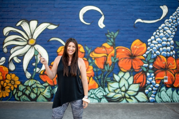 Maren Conrad stands with a paintbrush in front of one of her murals of flowers.
