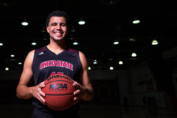 Malik Duffy holds a basketball between his hands with dramatic lighting behind him.