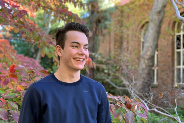 Chase Suihkonen smiles on campus, standing in front of trees transformed with fall colors.