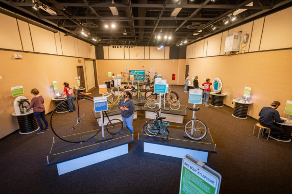 A museum space displays several different bicycles with a number of interactive displays against the walls.