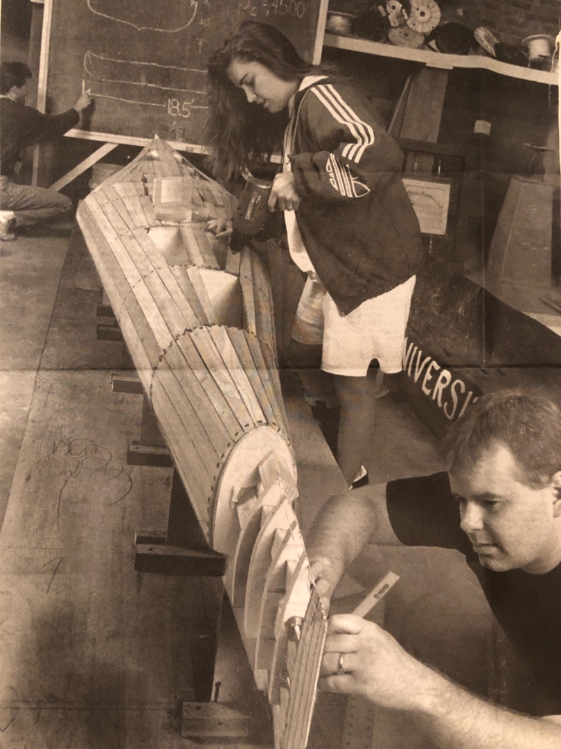 A black-and-white photo shows a young Julia working on building a concrete canoe with a classmate. 