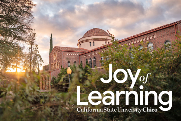 Clouds laden in sunlight float behind an academic building with the words "Joy of Learning, California State University Chico" in the foreground