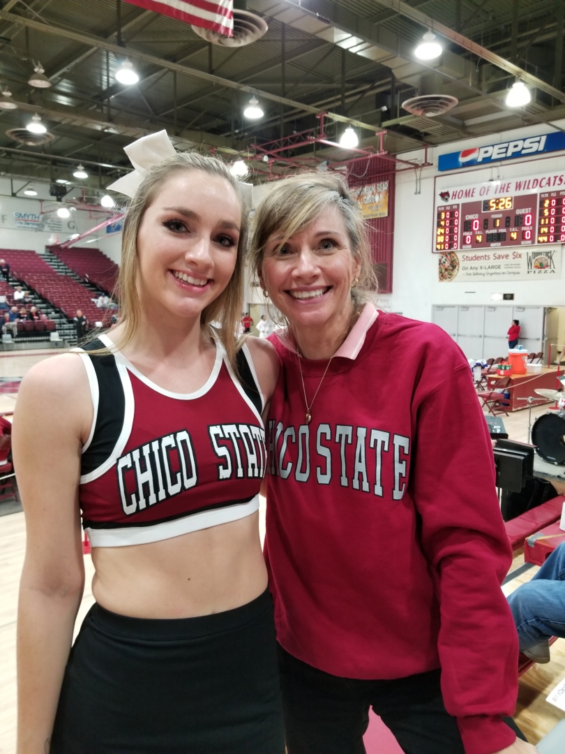 A daughter and mother smile as they stand in the crowd at a basketball game.