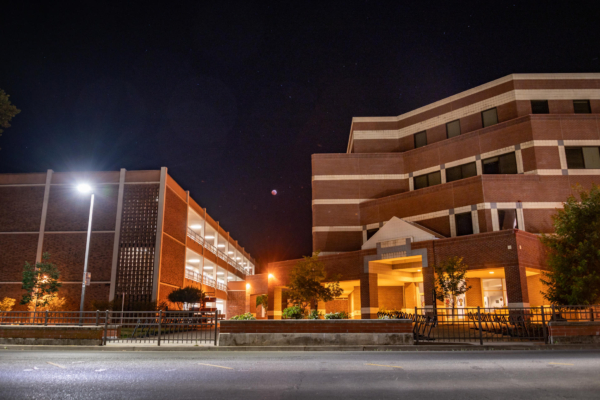 An eclipsed moon in a starry sky between two academic buildings