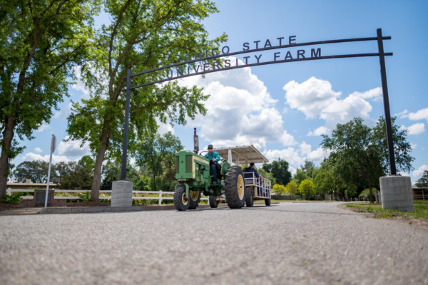 A college student drives a tractor beneath a sign that says Chico State University Farm