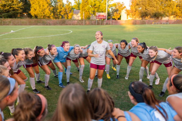 Susanna Garcia stands in a circle of soccer players who are standing arm in arm, getting pumped up at the start of a game.
