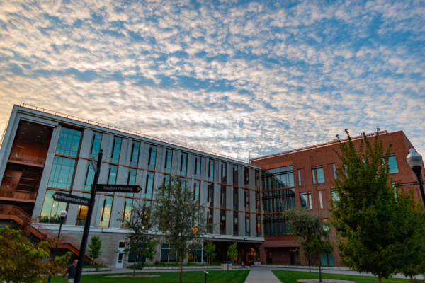 A sky is filled with clouds during a late afternoon sunset above a glass-facade academic building.