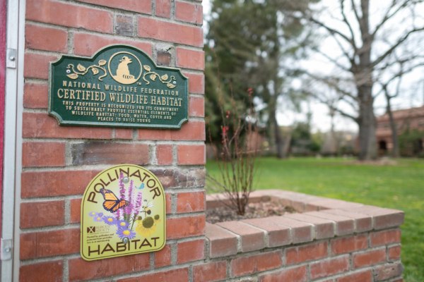 A pair of signs of designation as a Certified Wildlife Habitat and Pollinator Habitat on a brick facade