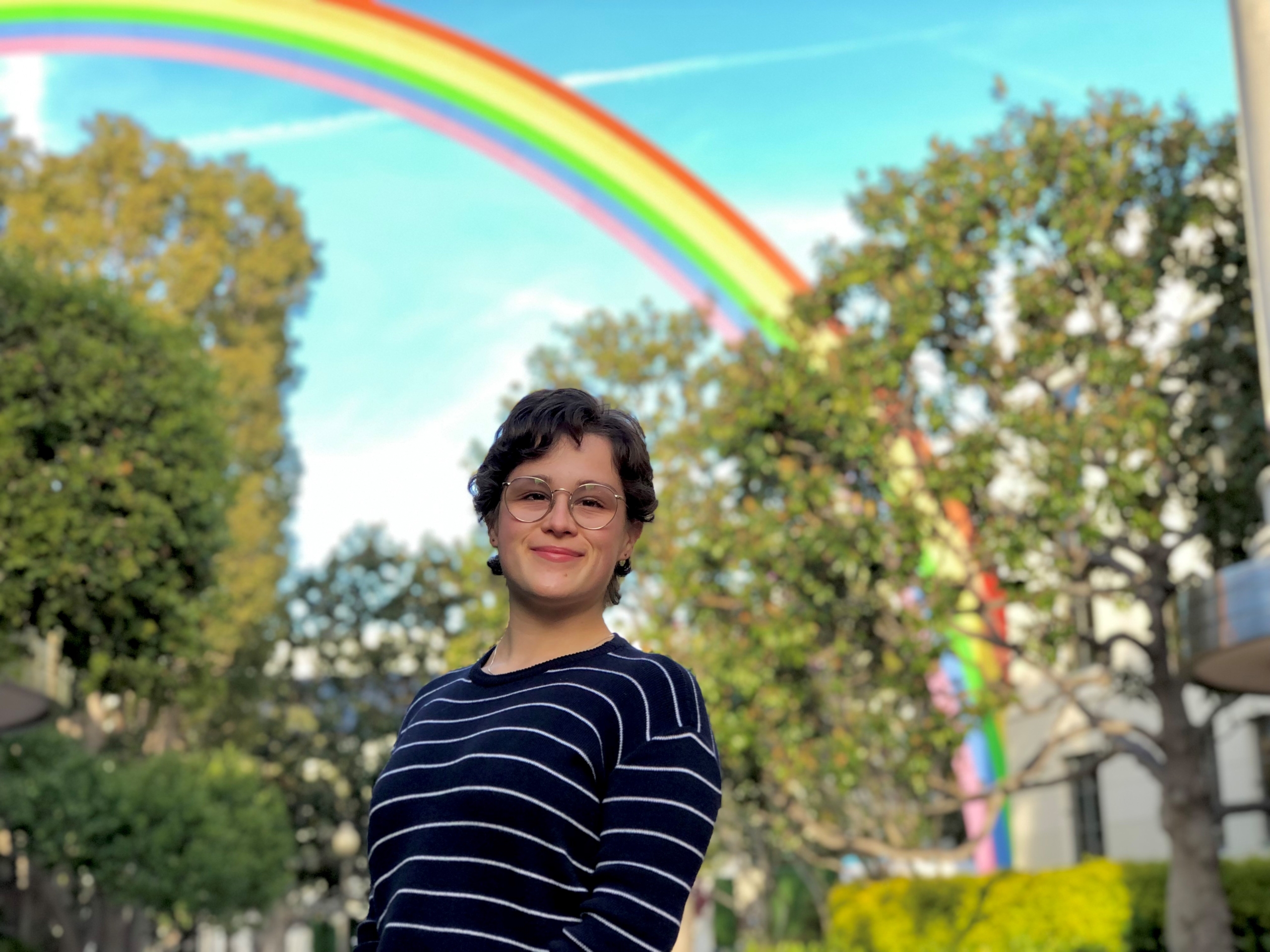 Hannah Hull photographed standing with trees and a rainbow structure in the background.
