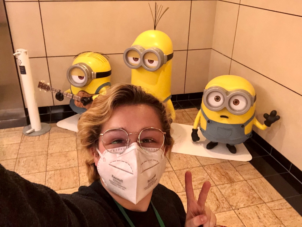 Hannah Hull stands in the foreground for a selfie making a peace sign with one hand while three minion cartoon figures can be seen in the background.