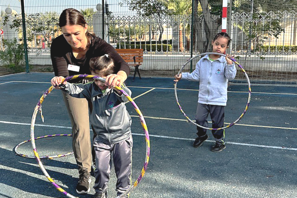 A Chico State educator interacts with children using hulahoops on a playground at a school in the UAE.
