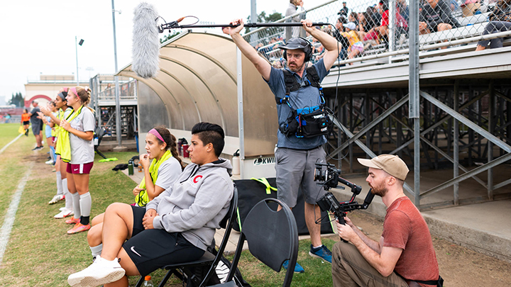 Chico State assistant coach Kat Benton-Laezza (right) and #6 Susanna Garcia (left) watch the action while being followed by a documentary crew during the Wildcats’ soccer match against Cal Poly Humboldt.