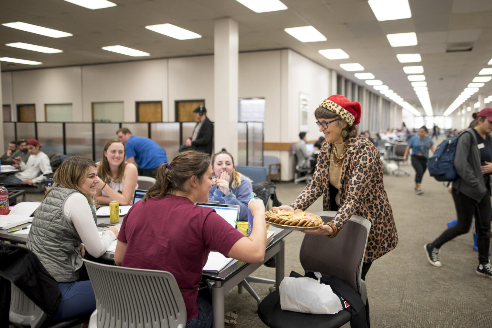President Hutchinson, dressed in a leopard-print jacket and Santa Hat, delivers cookies to students in the library during finals week.