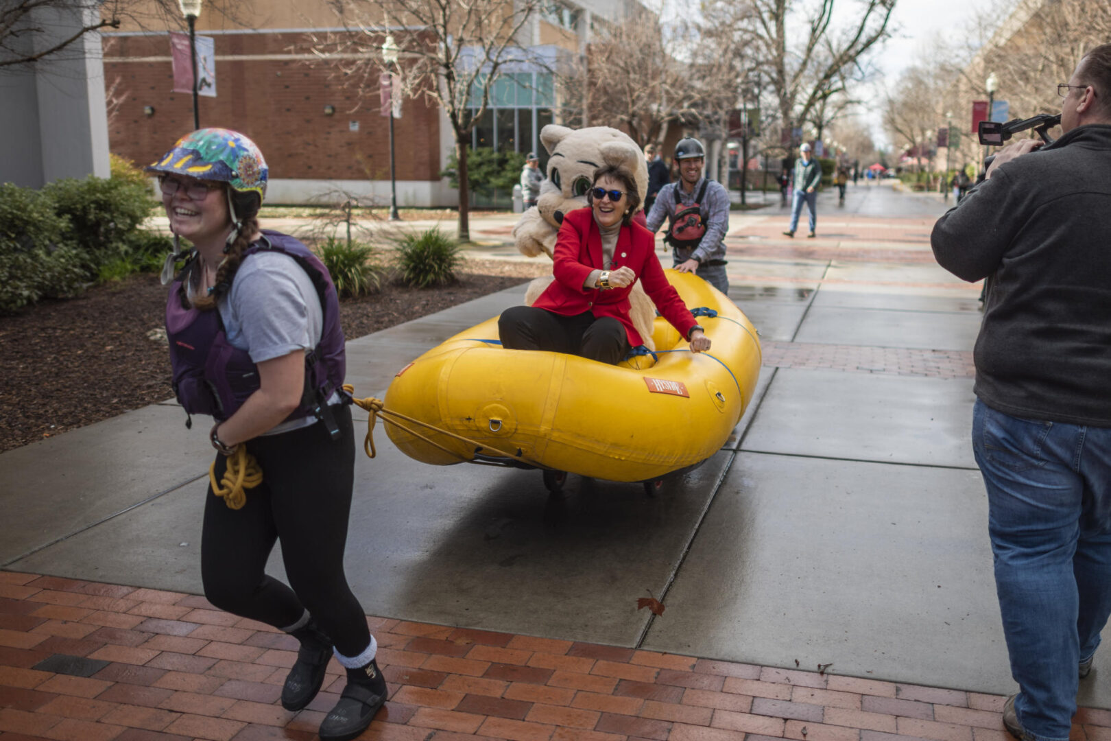 President Hutchinson laughs as she pretends to row while being pulled in a life raft on wheels by Adventure Outings staff on campus.