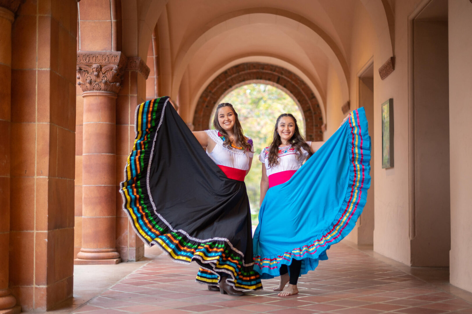 Twin sisters stand next to each other while holding out the skirts of their folklorico dresses. 