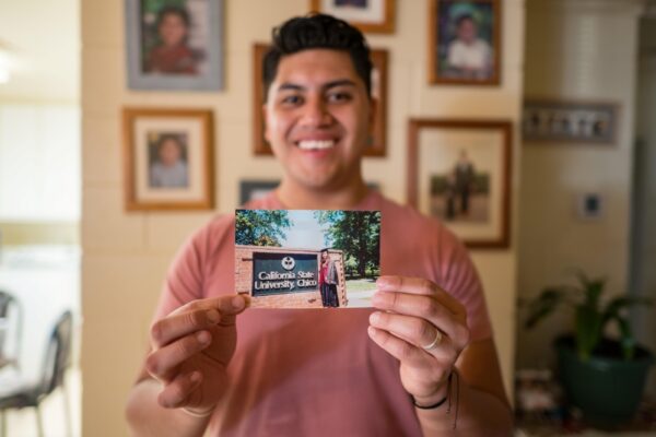 Eriberto Hernandez, who is out of focus, holds an old photograph of his older sister standing next to the Chico State sign and wearing a cap and gown.