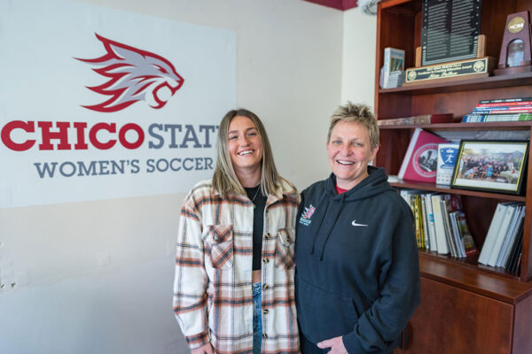 Mia Mendoza and Chico State Women's Soccer Coach Kim Sutton pose and smile in the women's soccer office.