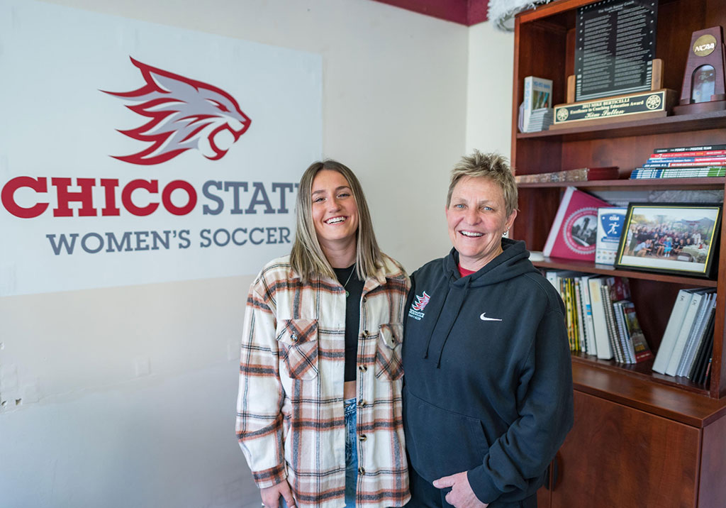Mia Mendoza and Chico State Women's Soccer Coach Kim Sutton pose and smile in the women's soccer office.