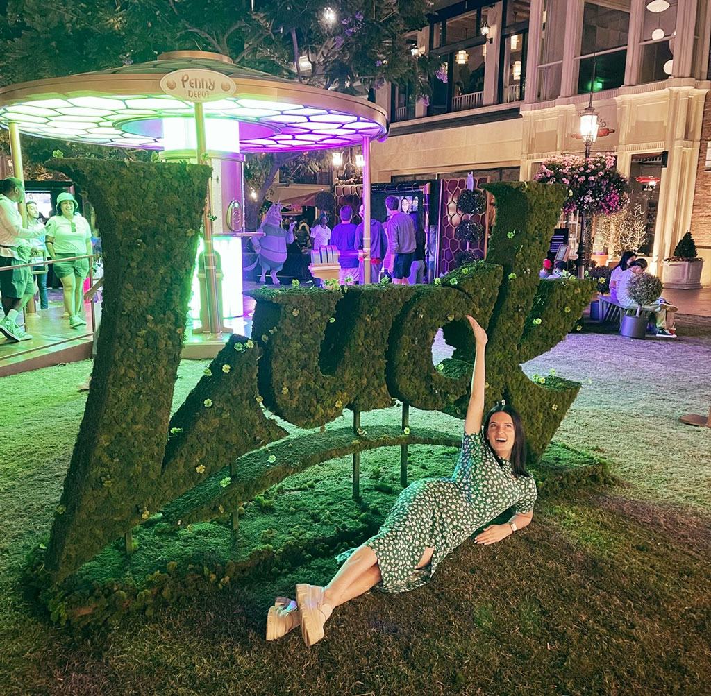Sophie McGuirk lays in front of a fake hedge shaped into the word "Luck" during the premiere activation event for the film at Disneyland,