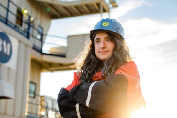 Irene Duran poses in high visibility safety gear and a hard hat on Iselin Dock in Woods Hole.