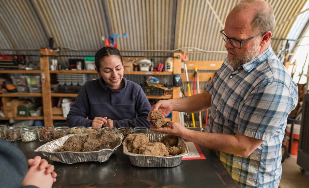 Johanna Jimenez (left) looks at a selection of soil and rock samples. To her right, Professor Garrett Liles inspects two rock samples.