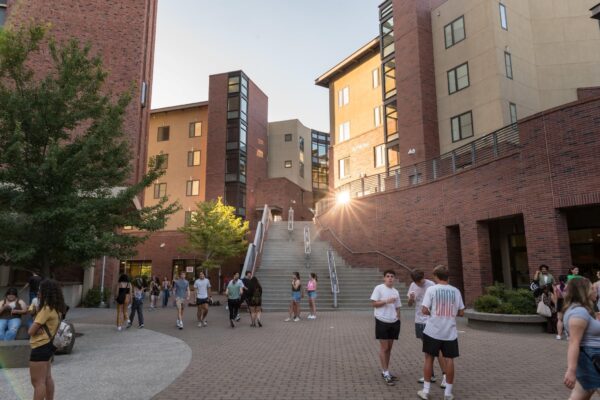 Students are seen walking and gathered around the courtyard between two brick buildings.