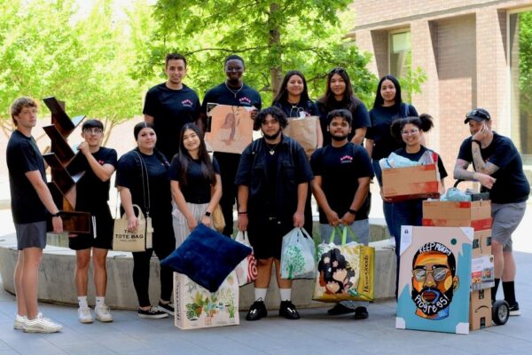 A group of students stands outdoors while holding bags and other household items to be donated to an emergency shelter run by Chico State's Basic Needs.