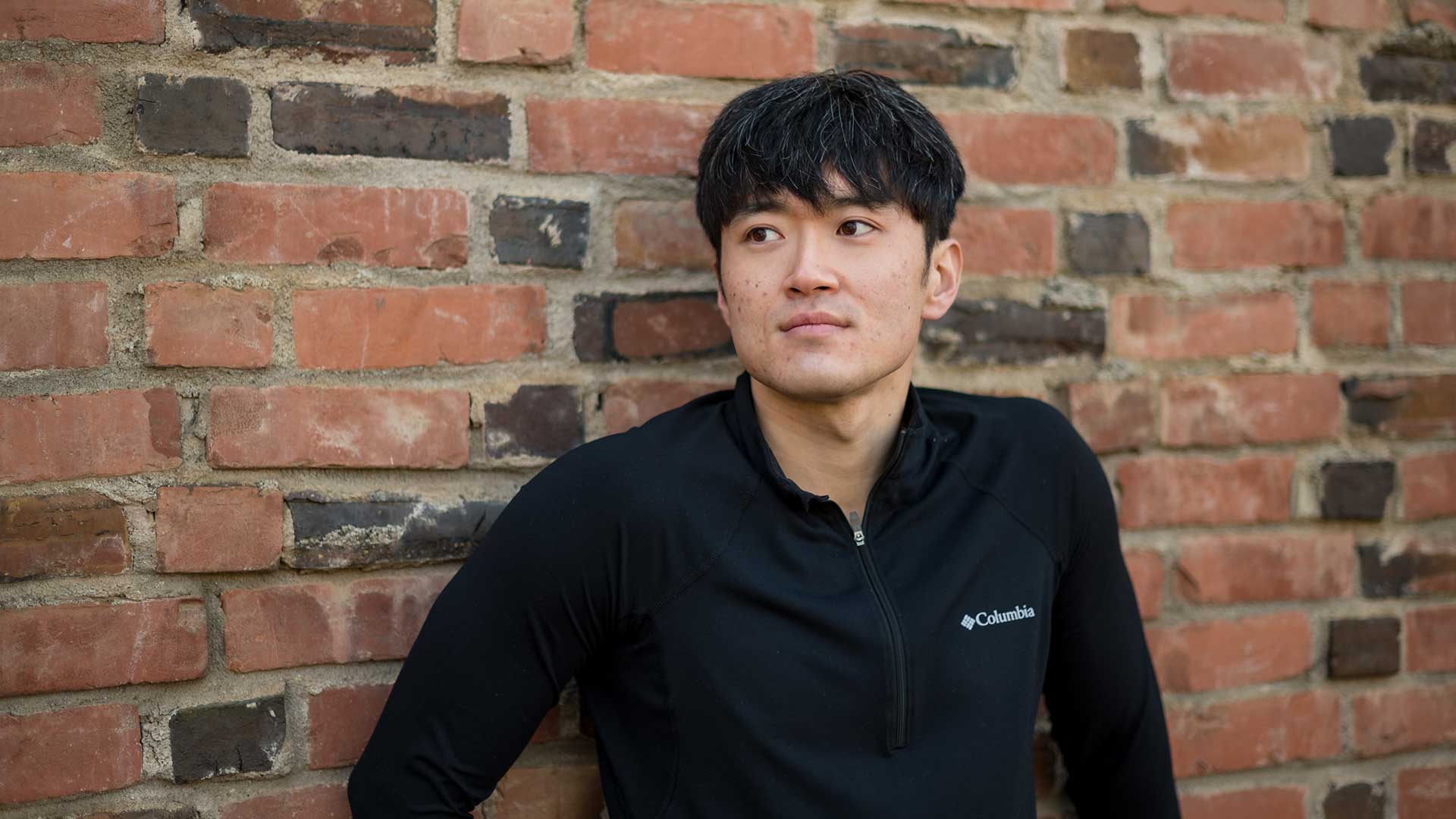 Haeryong Cheong is photographed against a facebrick wall, wearing a black seater.