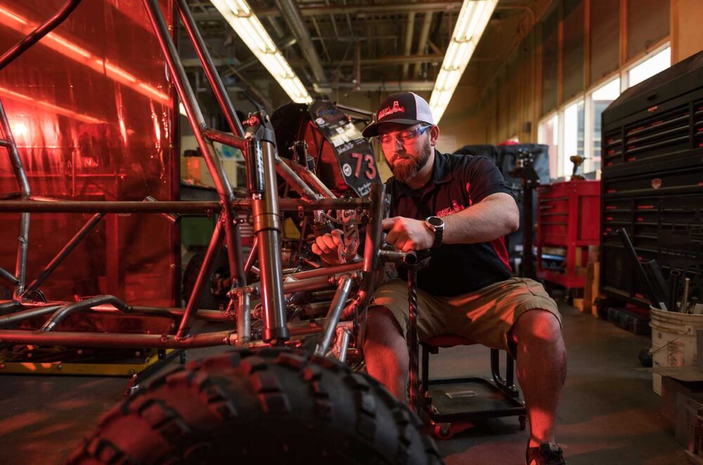 Alt text: Treyton Wood works on the Baja vehicle, wearing safety goggles.