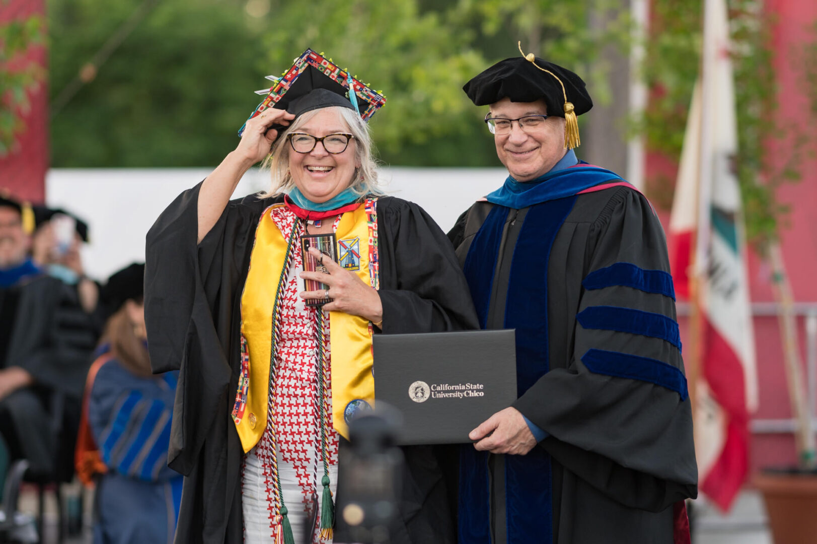 A graduating college student smiles and stands next to a dean of the college