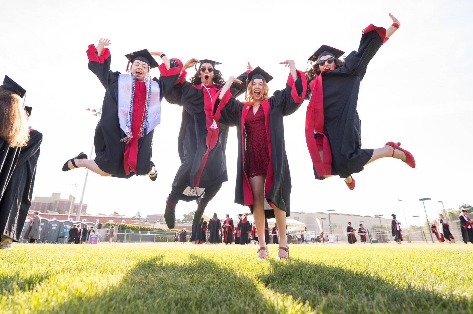 Four students wearing caps and gowns jump in unison celebrating their college graduation