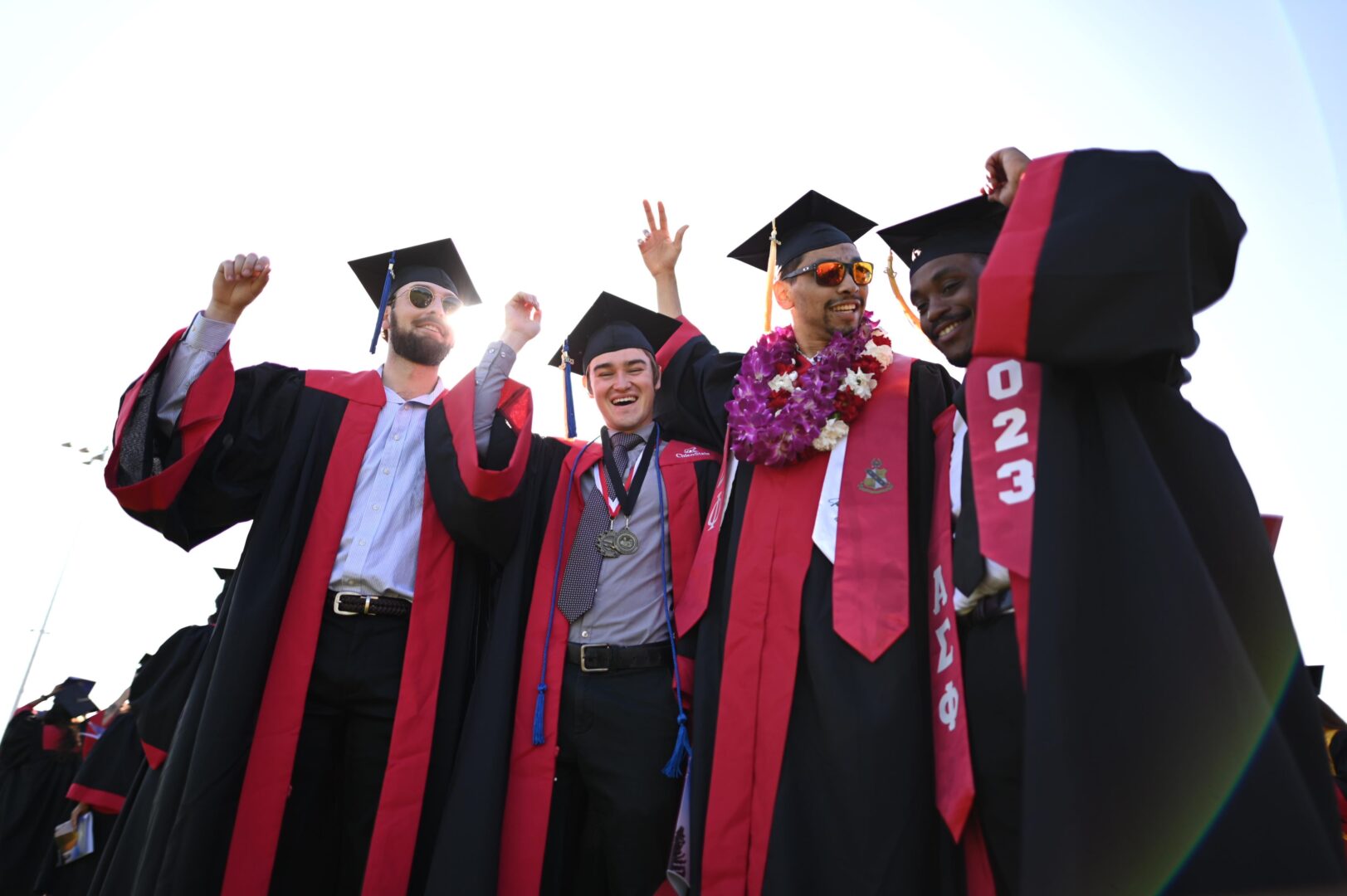 Four students wearing caps and gowns celebrate their college graduation.