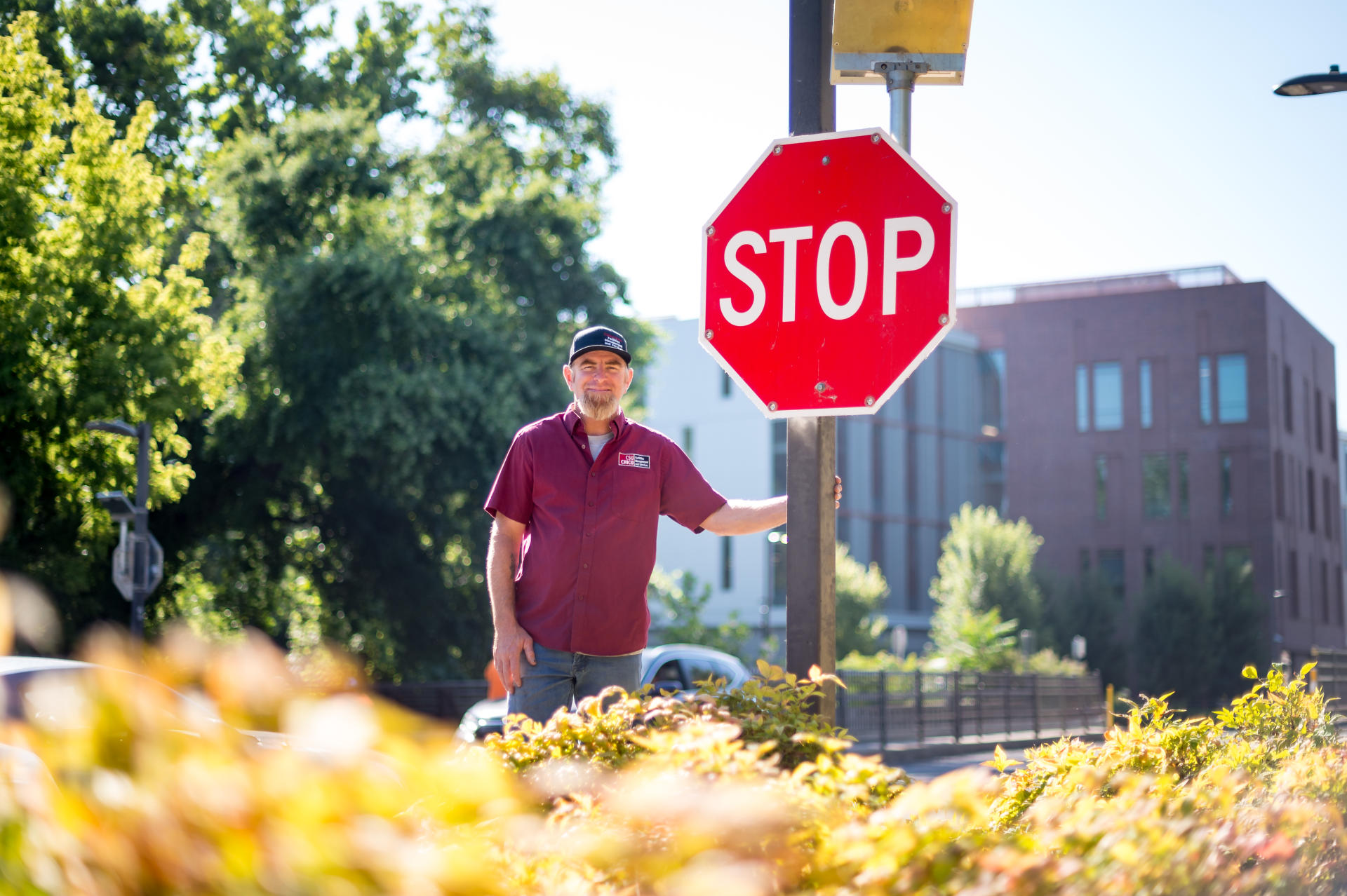Thomas DuSell stands next to the larger, lighted stop sign he pushed to have installed at the crosswalk along Warner Street and Ivy Street. The science building is in the background.