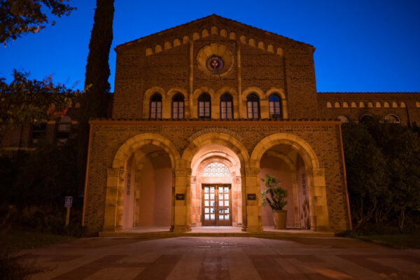 A lit doorway in front of an otherwise darkened academic building