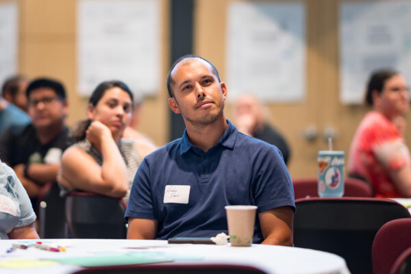 Student Jordan Davis sits at a table while attending a professional development event. He is wearing a navy blue polo shirt and a white name tag.