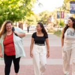 Three students laugh and smile as the walk down the promenade of campus.