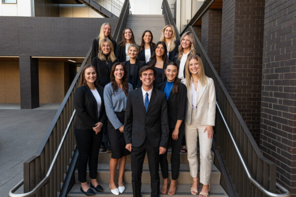 a group of student ins business casual wear stand on stairs for a photo.