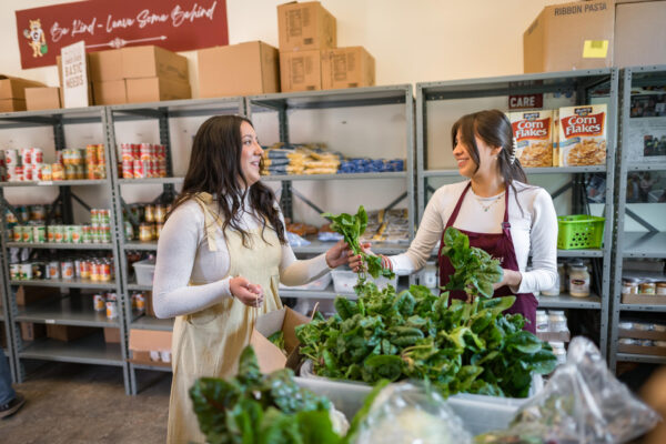 Two employees of a food pantry smile at each other and they distribute beautiful fresh produce