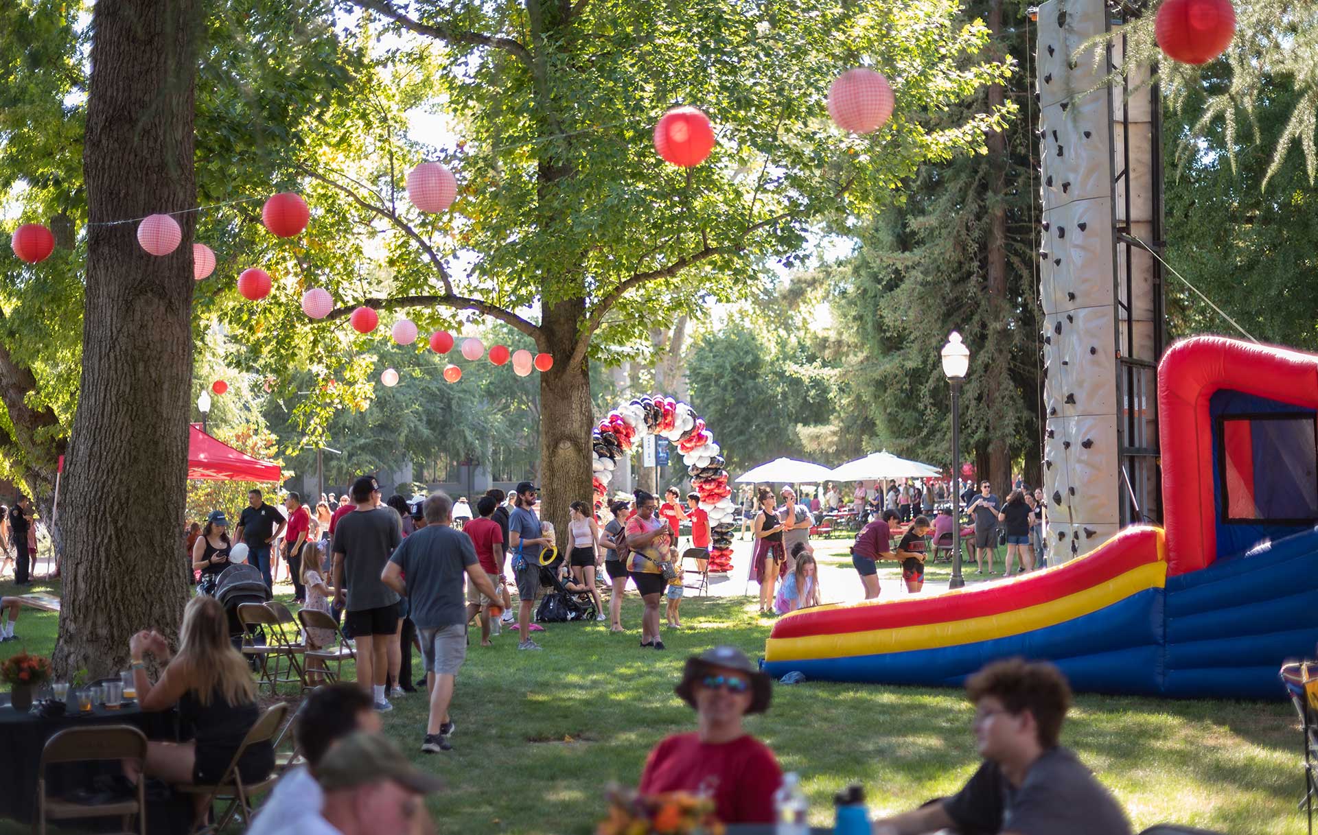 People are gathered on the lawn in front of Kendall Hall, which decorated with lights, balloons, and a bouncy house in honor of Homecoming Weekend.