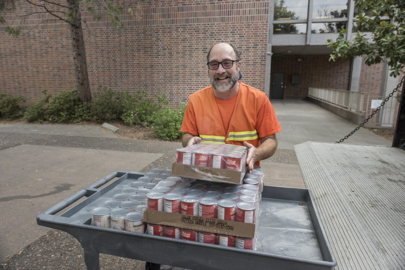 Joe Picard, wearing an orange shirt, places packages of tomato sauce on a cart.