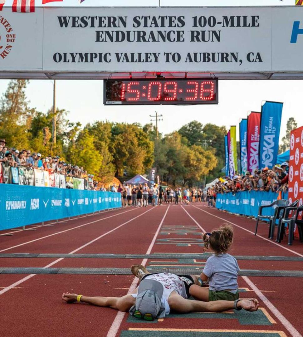 Anthony Costales lays on the ground just beyond the finish line of the Western States 100 as his daughter, Piper, sits next to him.
