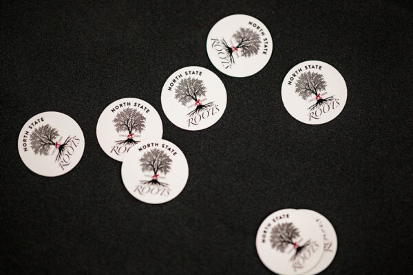 Stickers that show the North State Roots logo are scattered across a black tablecloth.