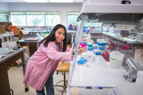 Donning her pink lab coat, microbiology major Nayellie Barragan-Mejia smiles for the camera while conducting research at a lab at Chico State.