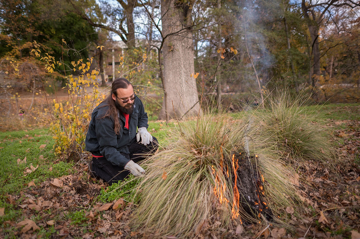 He-Lo Ramirez crouches on his knees to ignite a clump of deergrass on the Chico State campus.